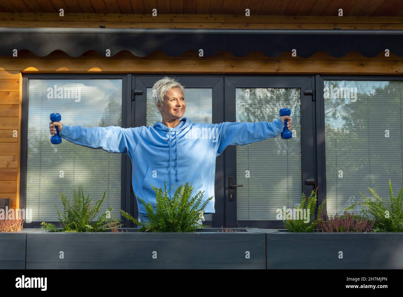Happy woman exercising with dumbbells on patio Stock Photo