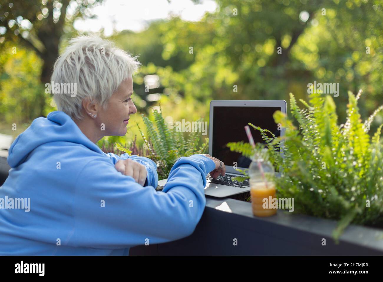 Woman with juice working at laptop on patio Stock Photo