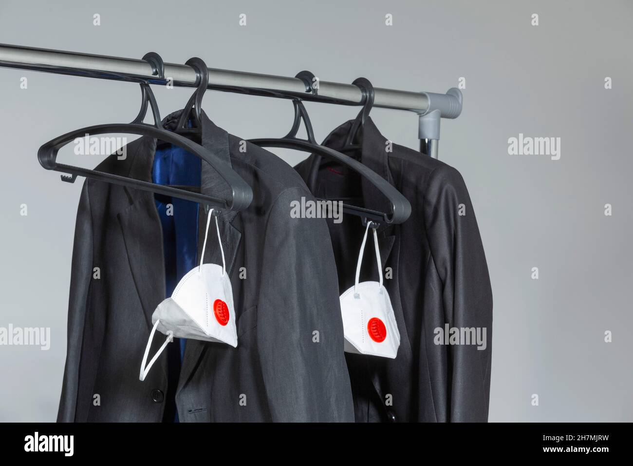 Business suit jackets and protective face masks hanging on rack Stock