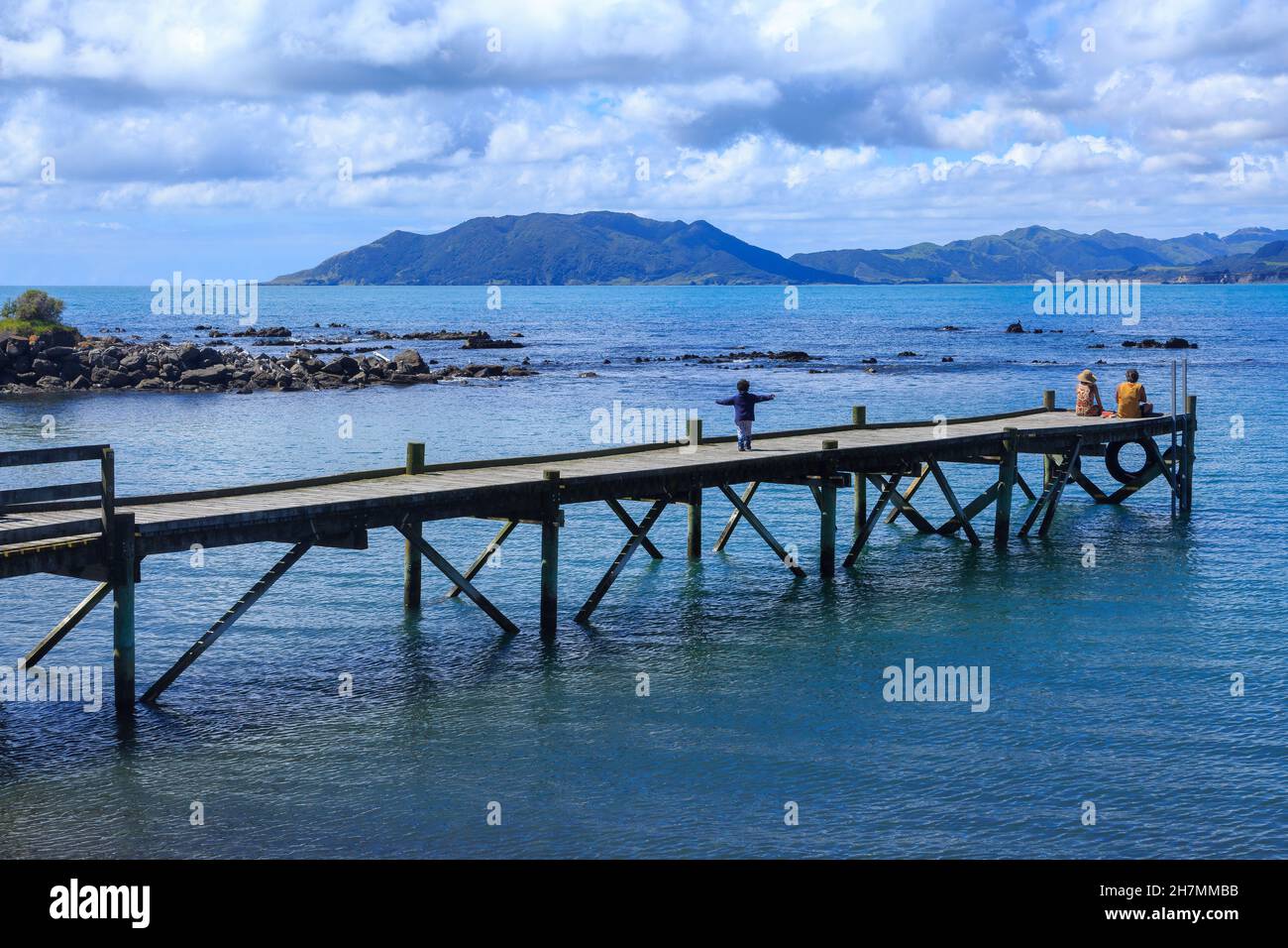 A pier at Waihau Bay, New Zealand, with a view of Cape Runaway, the easternmost point in the Bay of Plenty Stock Photo