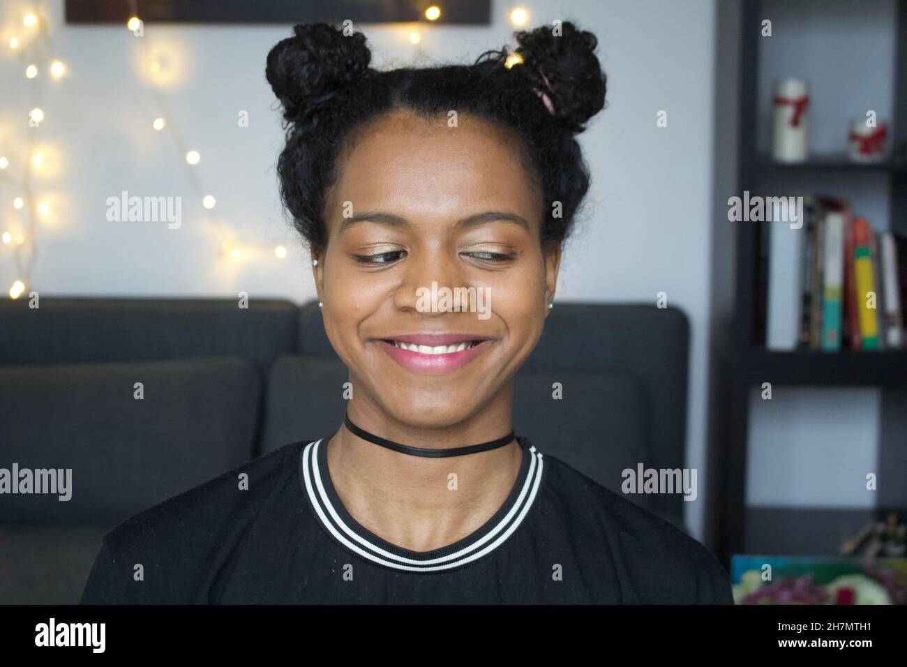 Black girl with space buns smiling whilst glancing sideways, off camera. Stock Photo