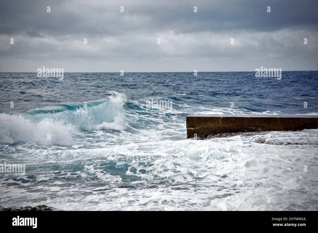 Wave rolling to the small stone pier with horizon line in background.Wave on Adriatic Sea on Croatian coastline with horizon line in background. Storm Stock Photo