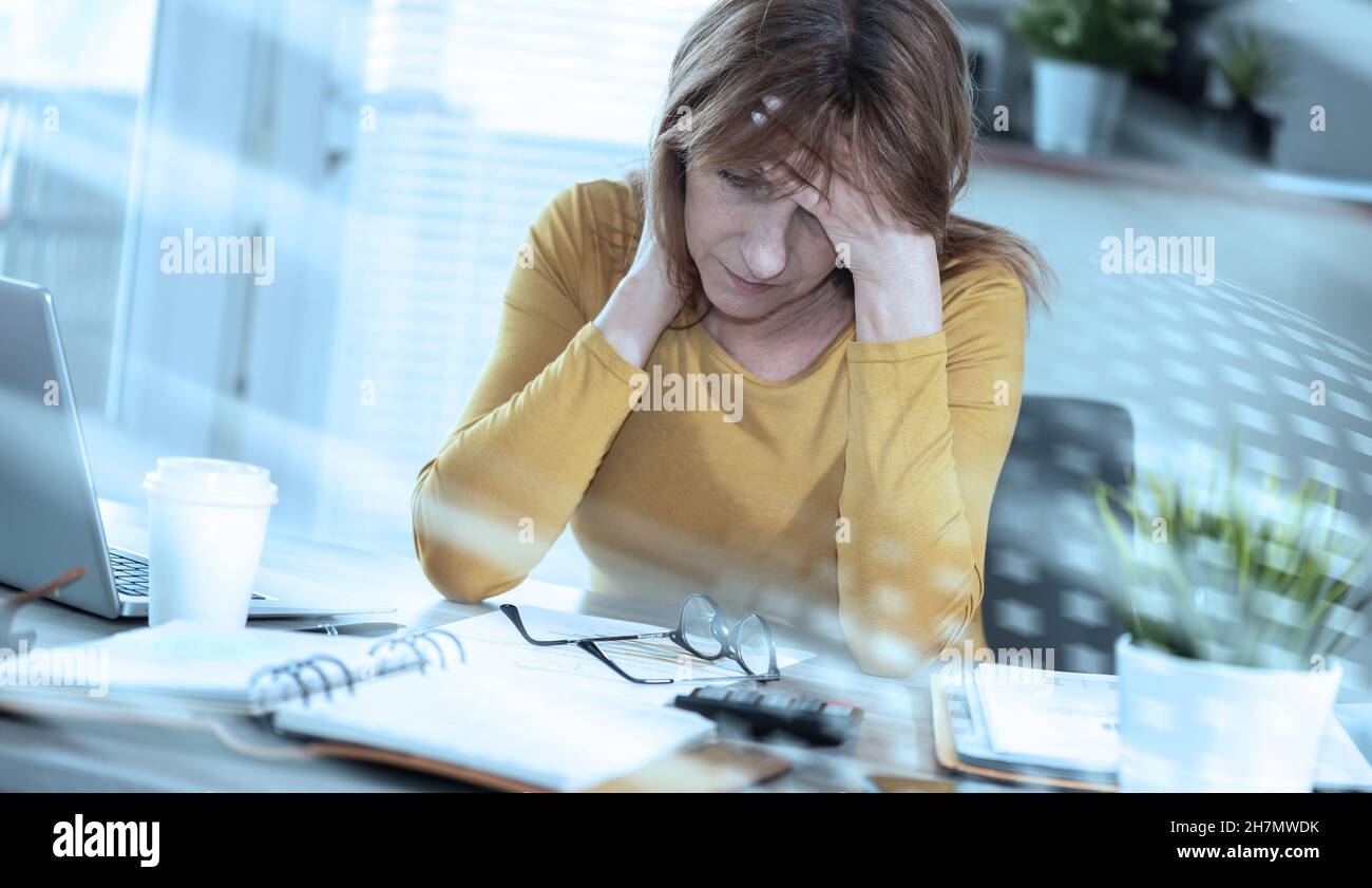 Stressed businesswoman sitting in office with hand on forehead; light ...