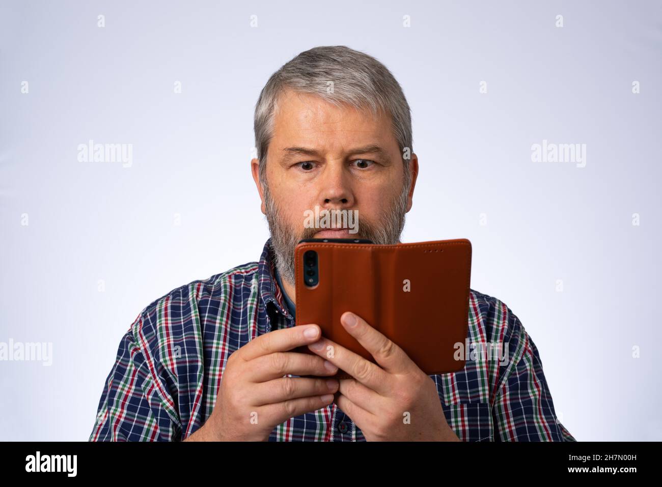 Man with full beard, 54 years old, looks shocked, stunned at his smartphone Huawei P20 pro Stock Photo