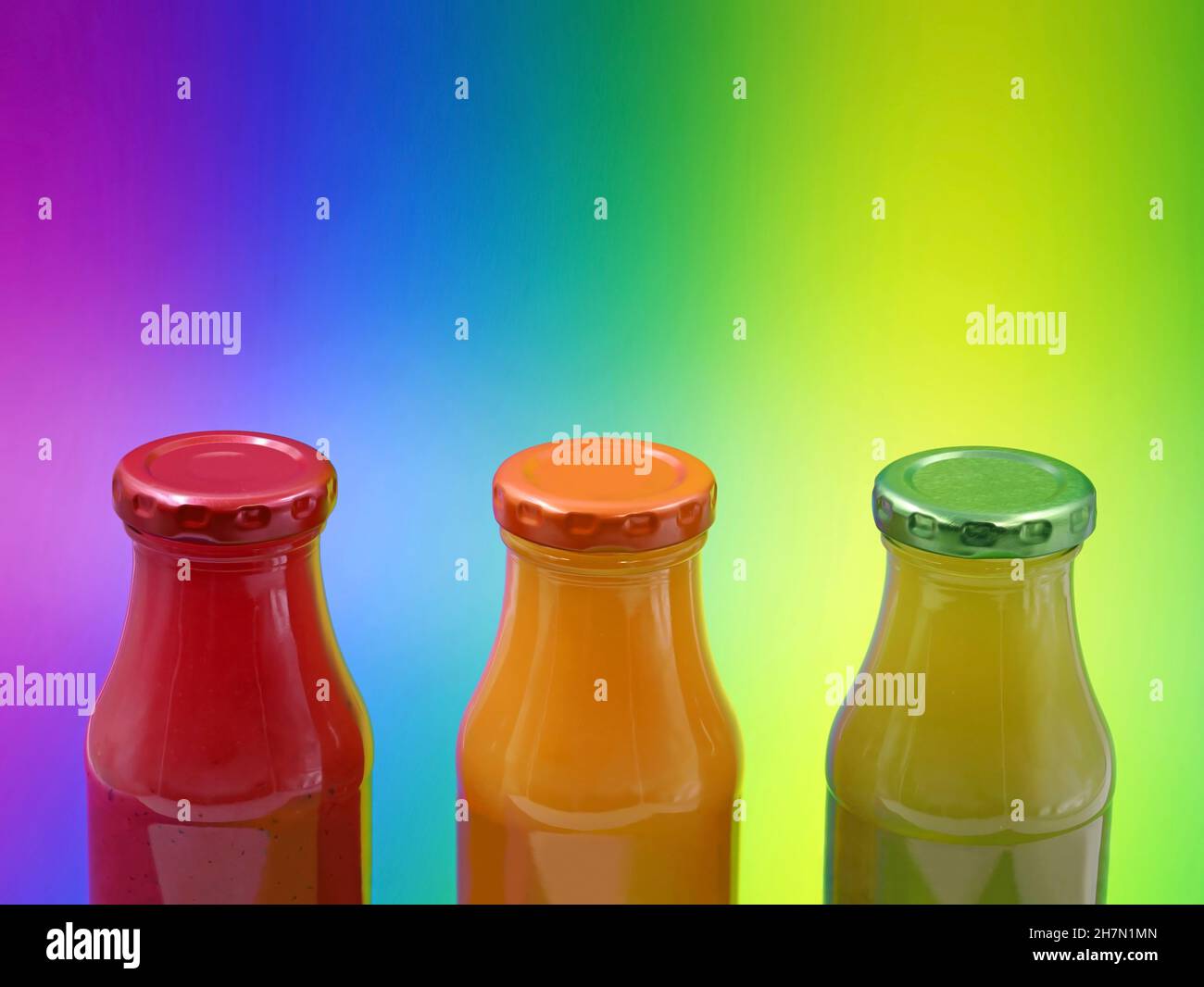 glass bottles with healthy smoothies on multicolored background with copy space, close up of red, orange and green fuit juice bottles Stock Photo