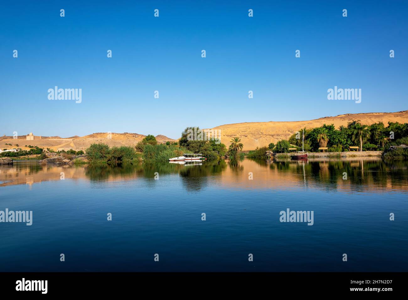 Sand dunes and palm trees reflected in the Nile River in Aswan, Egypt Stock Photo