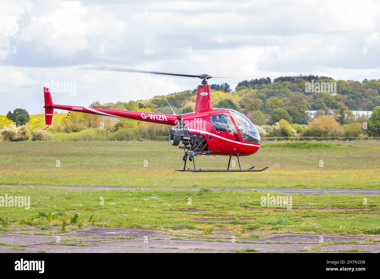 Side view of pilot inside red R22 Beta II helicopter taking off from Halfpenny Green airfield, UK, locally known as Bobbington Airport. Stock Photo