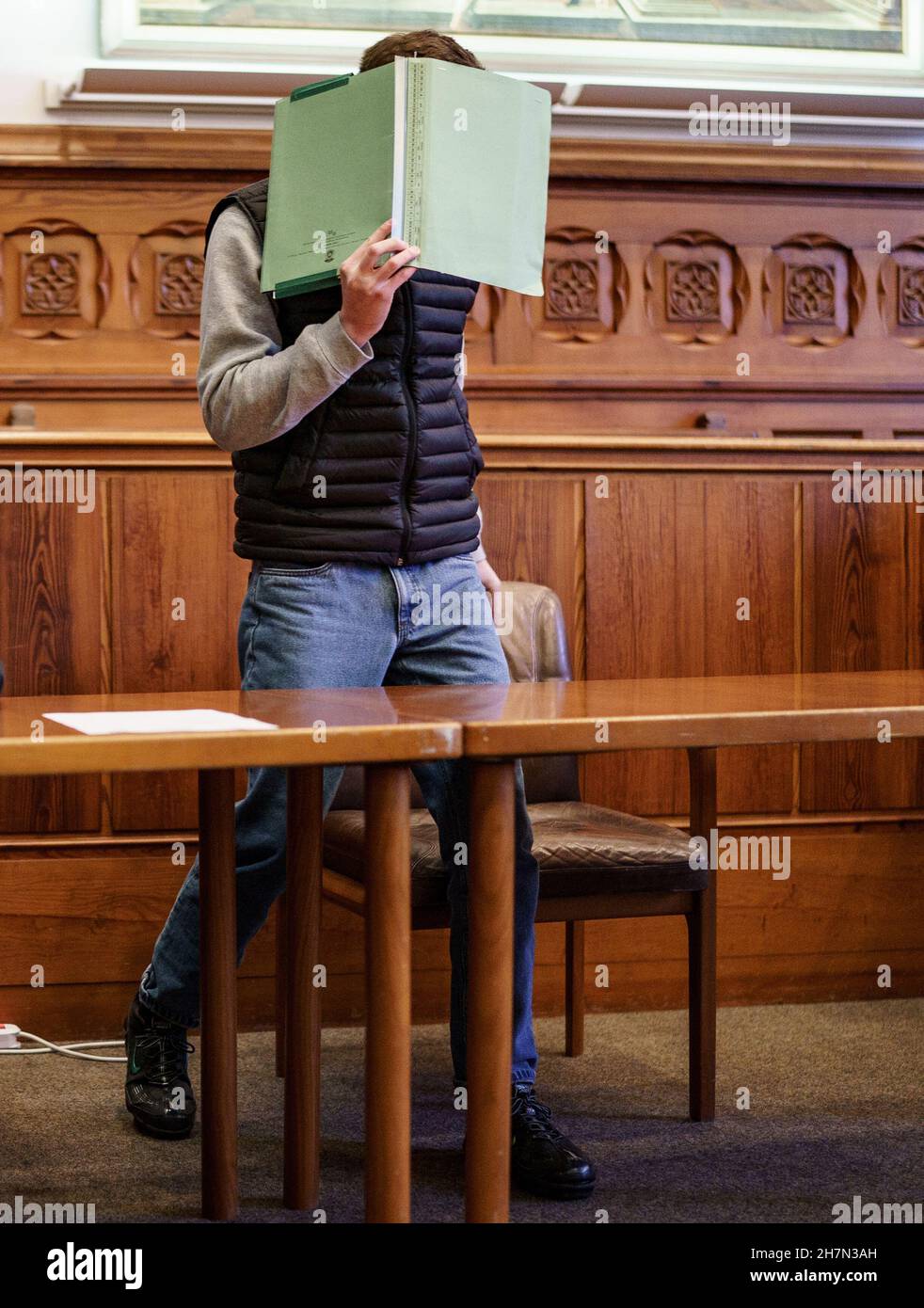 Flensburg, Germany. 24th Nov, 2021. The 20-year-old defendant in the manslaughter trial is waiting in the courtroom for the verdict to be announced. The young man is alleged to have stabbed a 16-year-old to death on 2 April 2021 after an argument on a viewing platform near the Duborgskolen in Flensburg. Credit: Axel Heimken/dpa/Alamy Live News Stock Photo
