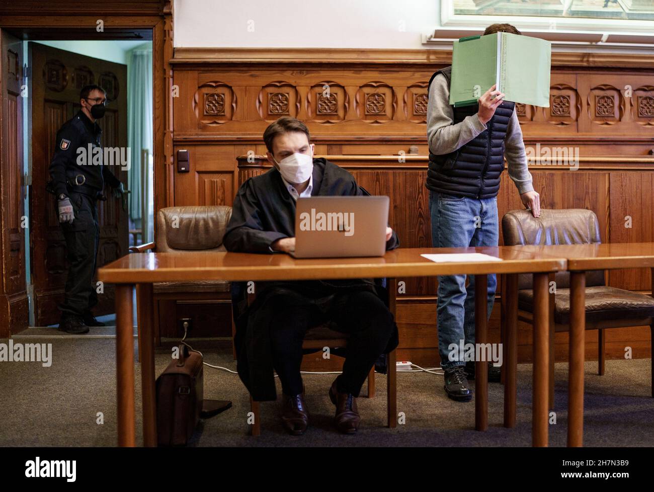 Flensburg, Germany. 24th Nov, 2021. The 20-year-old defendant in the manslaughter trial waits in the courtroom next to his lawyer Christian Steinhardt (M) for the verdict to be announced. The young man is alleged to have stabbed a 16-year-old to death on 2 April 2021 after an argument on a viewing platform near the Duborgskolen in Flensburg. Credit: Axel Heimken/dpa/Alamy Live News Stock Photo
