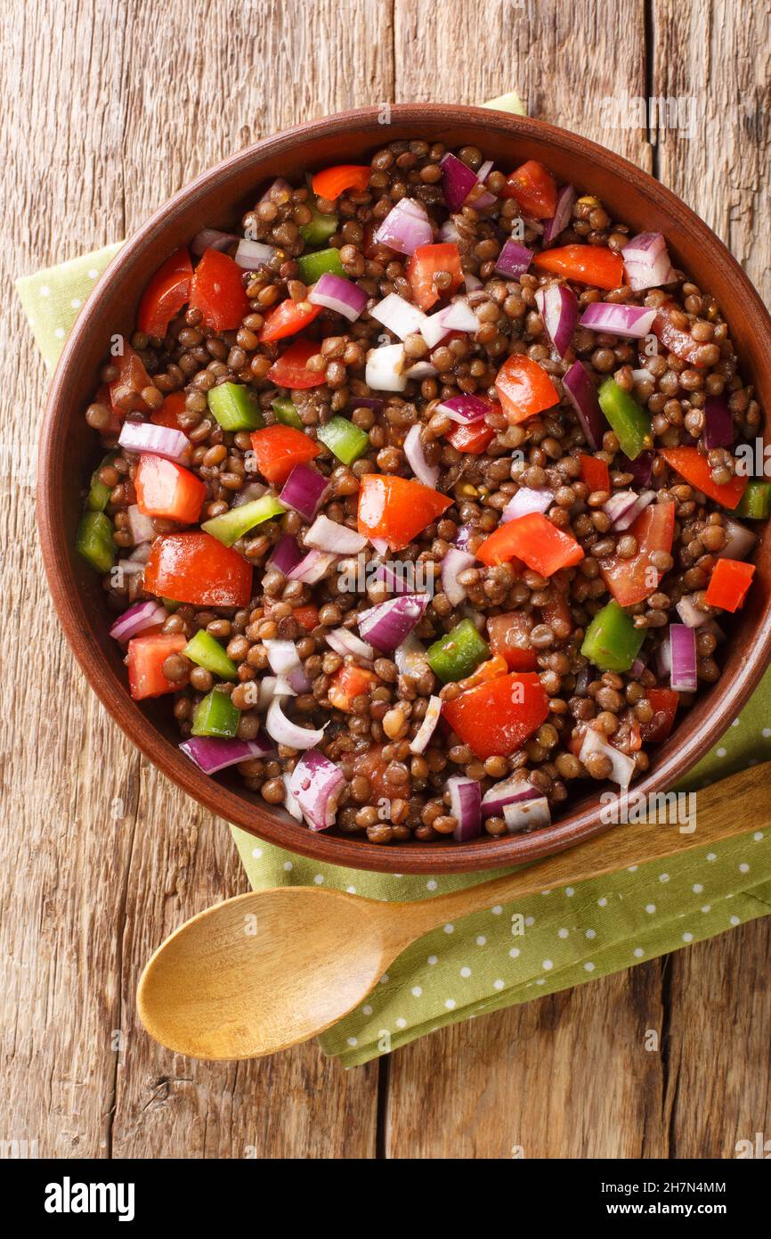 Green lentil salad with tomatoes, onions and chili peppers close-up in a plate on the table. vertical top view from above Stock Photo