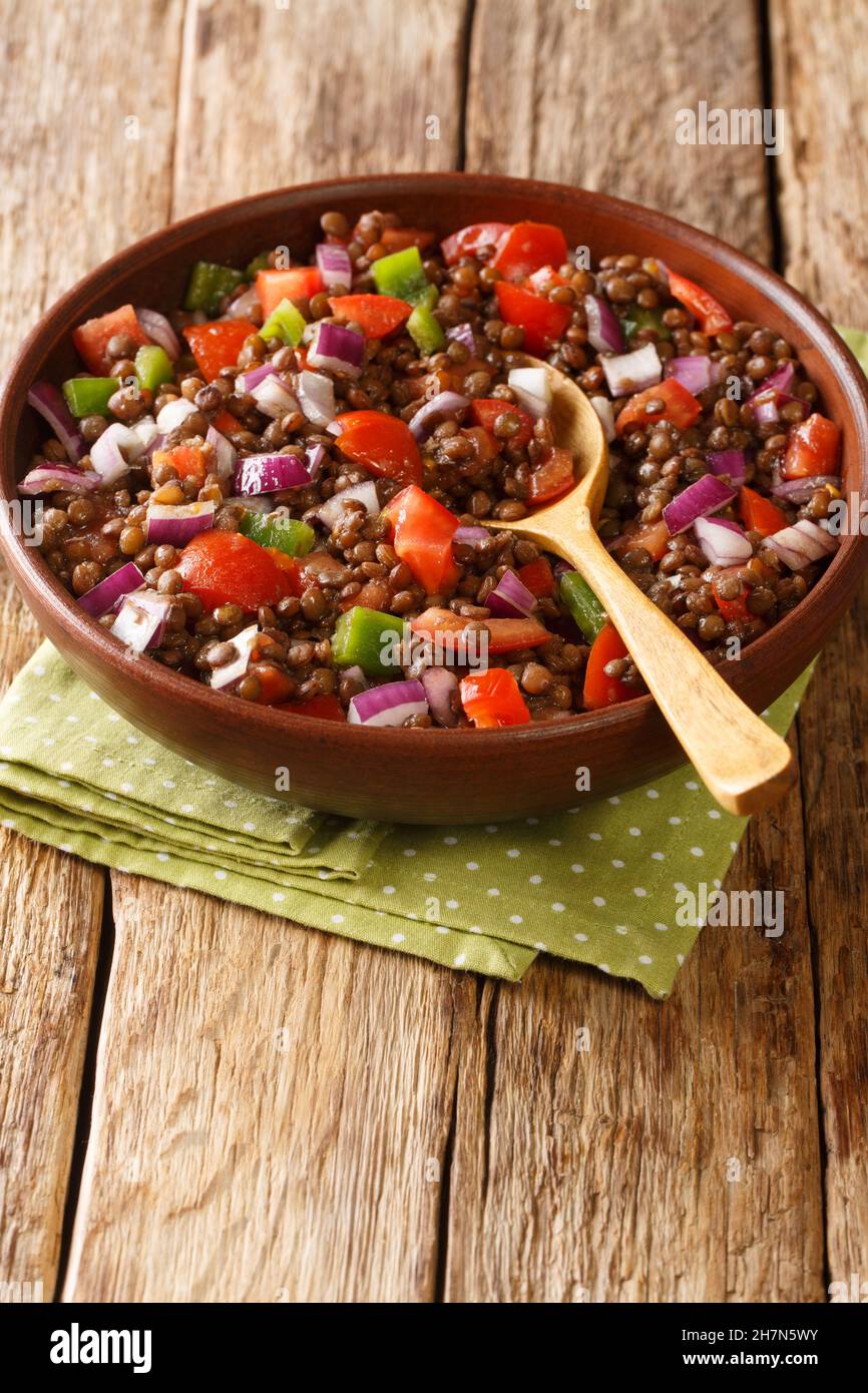 Green lentil salad with tomatoes, onions and chili peppers close-up in a plate on the table. vertical Stock Photo