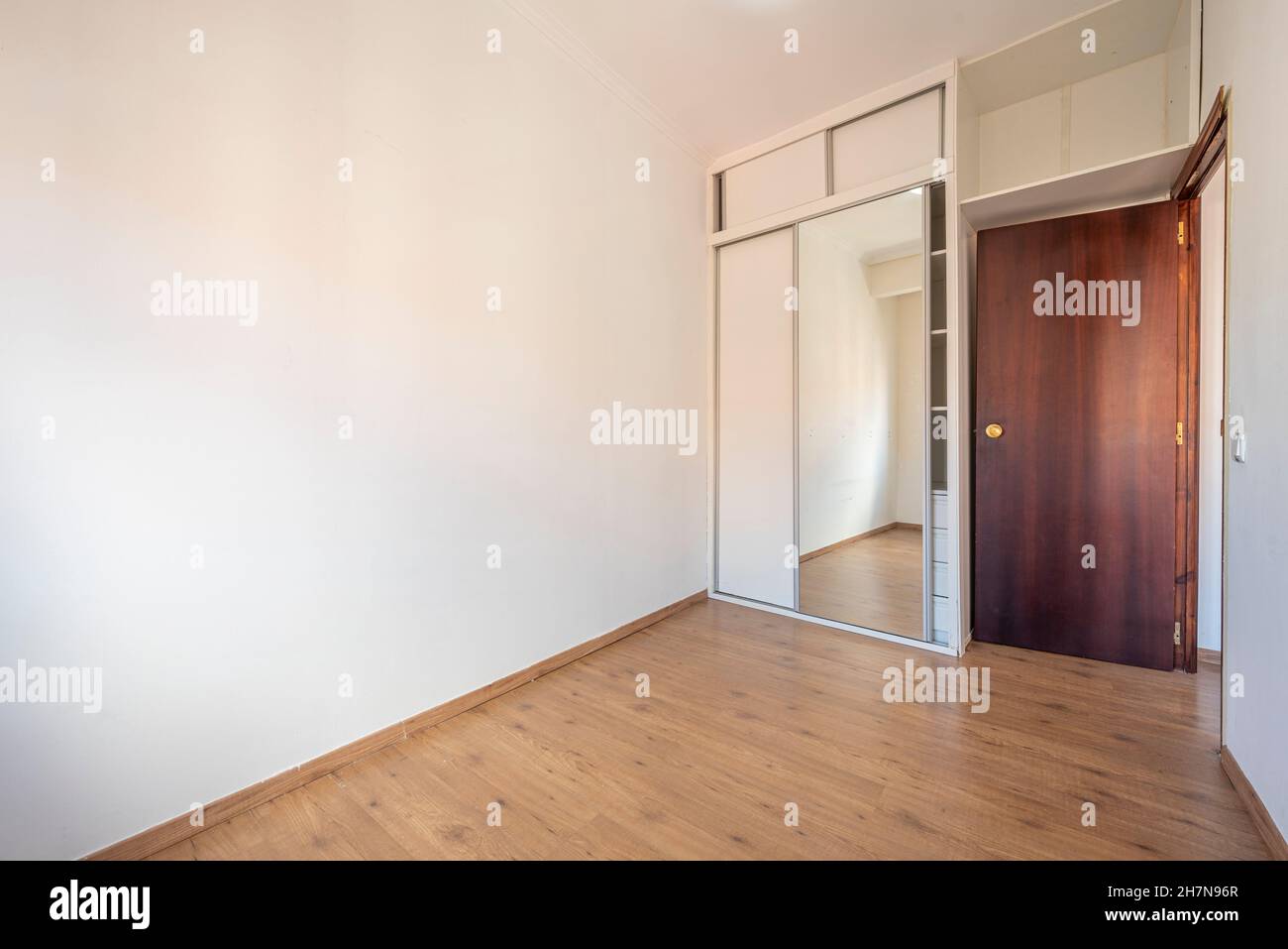 Conventional bedroom with built-in wardrobe with a mirrored door and white chest of drawers Stock Photo