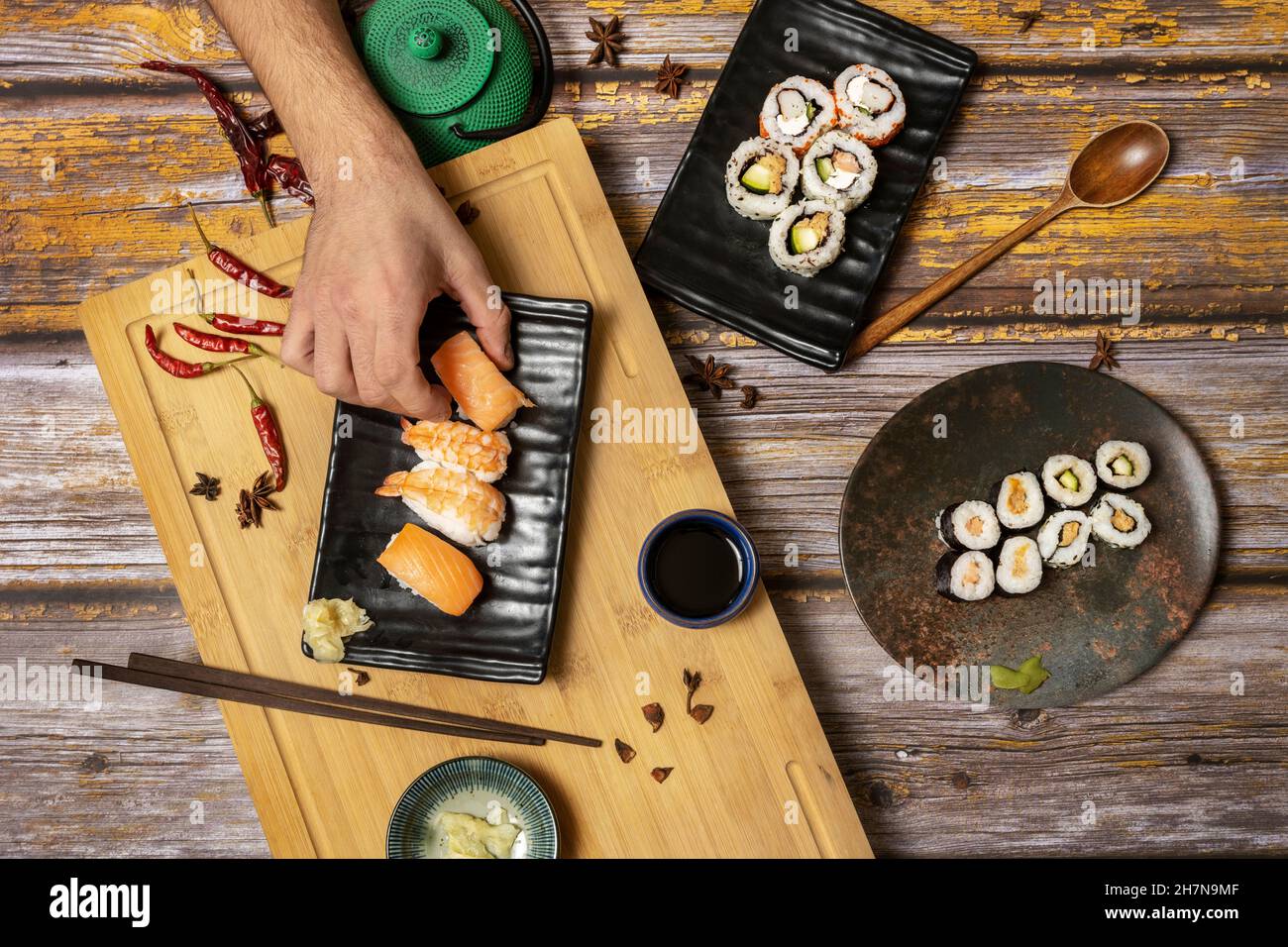 Man's hand holding a piece of Norwegian salmon nigiri sushi from a set of Japanese food dishes with chopsticks and soy sauce Stock Photo