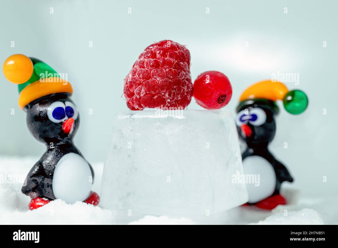 A pair of penguins made from Venetian glass in front of raspberry and red currant on the ice cube. Animal figurines made from Murano glass. Handmade. Stock Photo