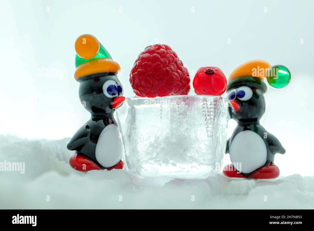A pair of penguins made from Venetian glass in front of raspberry and red currant on the ice cube. Animal figurines made from Murano glass. Handmade. Stock Photo