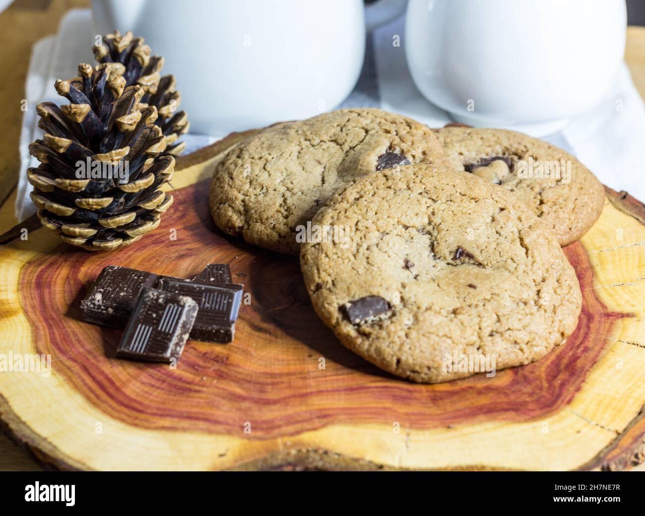 Chocolate Chip Cookies on Log Wooden Board Served with Chocolate Pieces and Tea Decorated with Pine Cone. Selective Focus Stock Photo