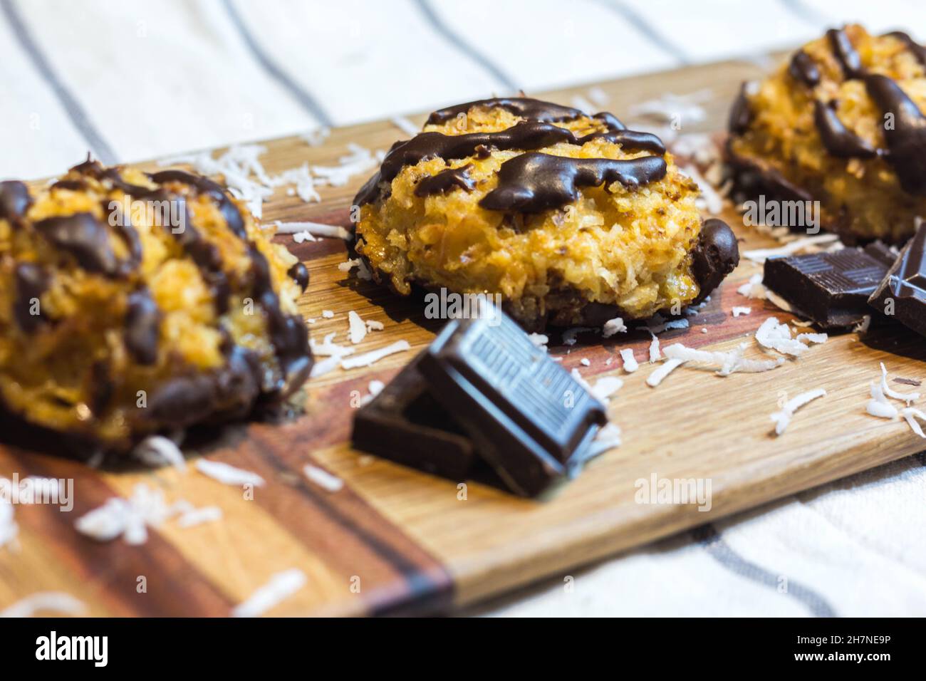 Close up of Coconut Macaroons with Dark Chocolate Drizzle Served on Wooden Serving Board Garnished with Chocolate Pieces and Coconut Shavings. Selecti Stock Photo