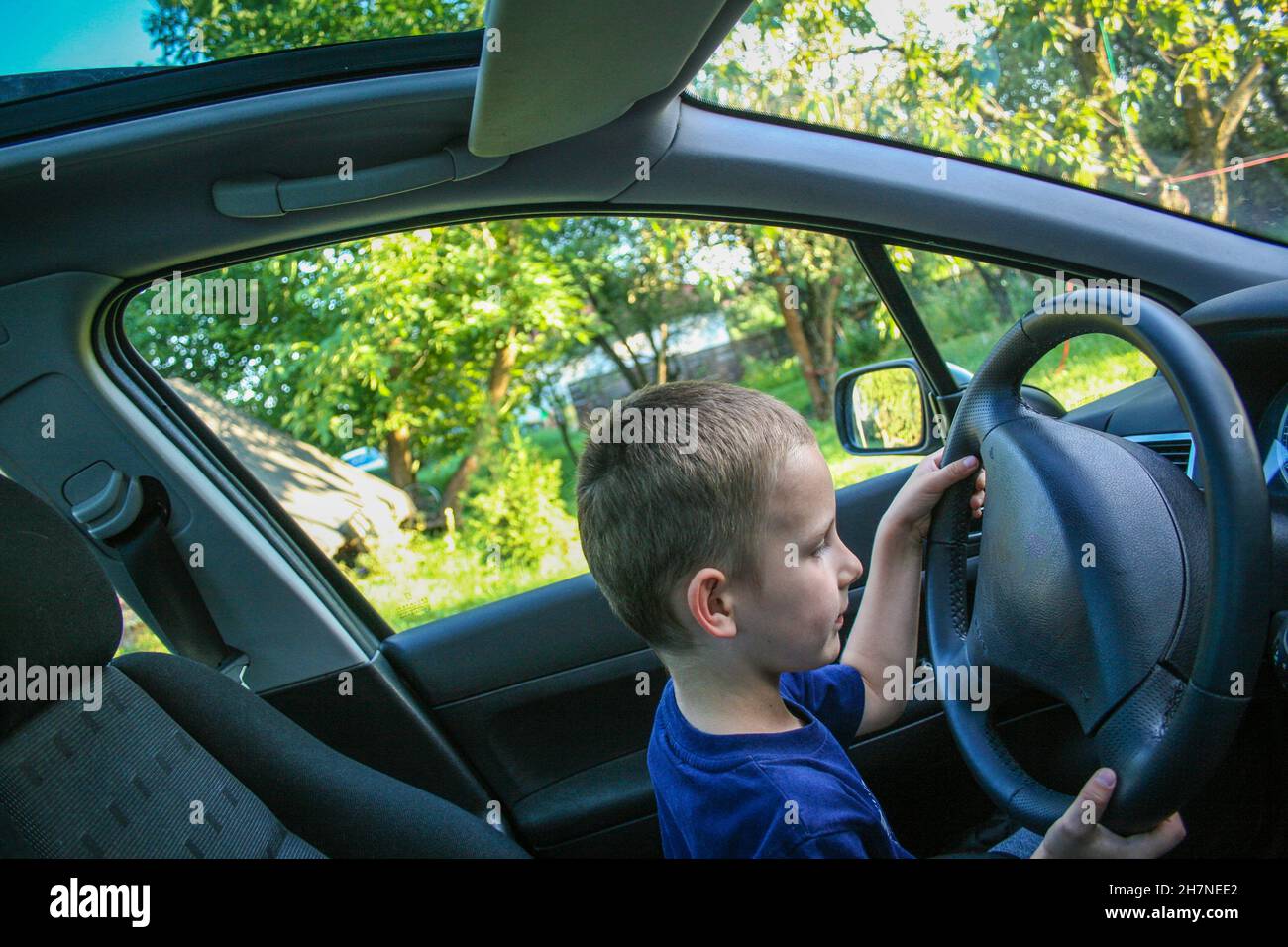 Four years old baby boy sit behind the wheel and pretend driving car Stock Photo