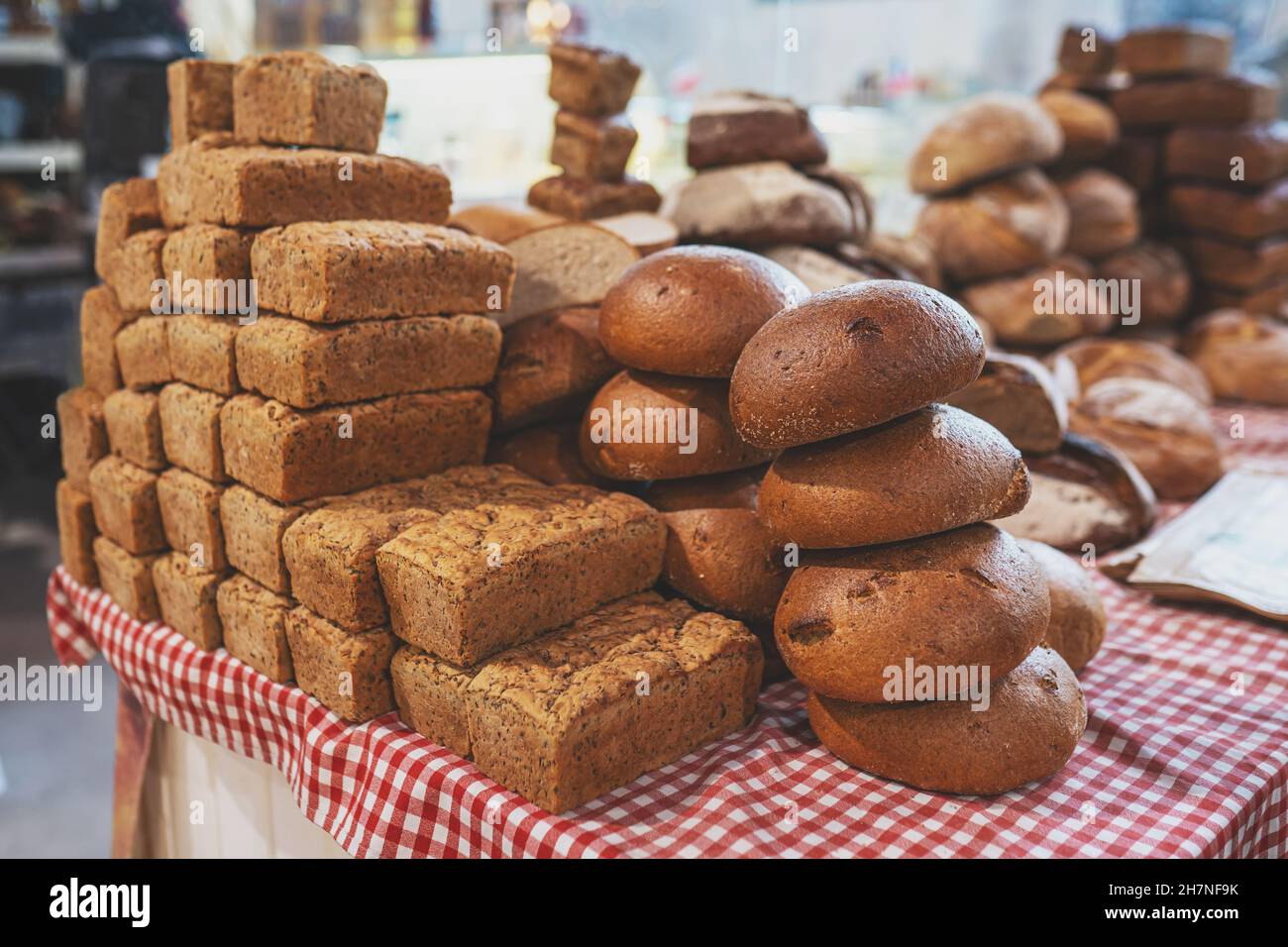 Pile of freshly baked loaves of bread on table at the local market. Many traditional fresh round and square bread loaves for sale. No people. Selective focus. Stock Photo