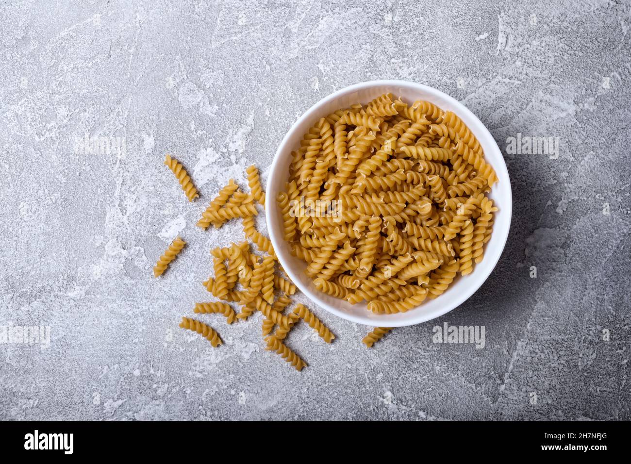 Top view of italian raw rotini pasta in white bowl on grey concrete background Stock Photo
