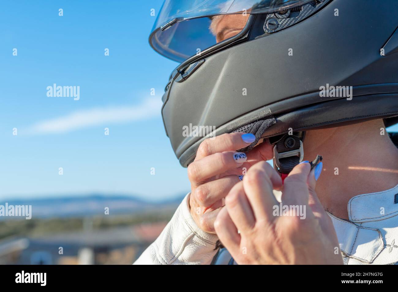 young female biker fastening her safety helmet to ride a motorcycle. safety and protection concept on the road Stock Photo