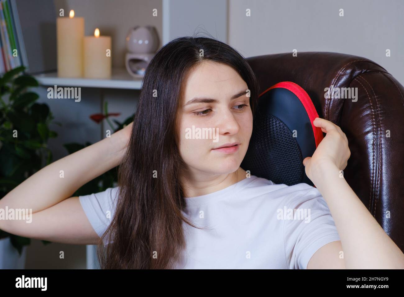 A woman sits in a chair with a massage pillow and does a neck massage
