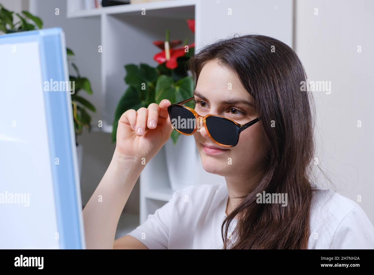 A woman looks at a computer screen through perforated glasses with