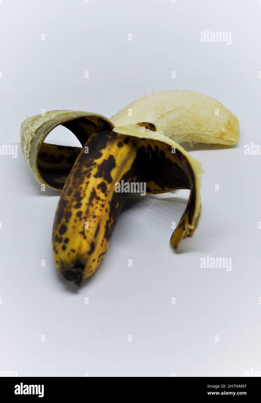 Cut out image of an over ripe banana which is half peeled set against a white background Stock Photo