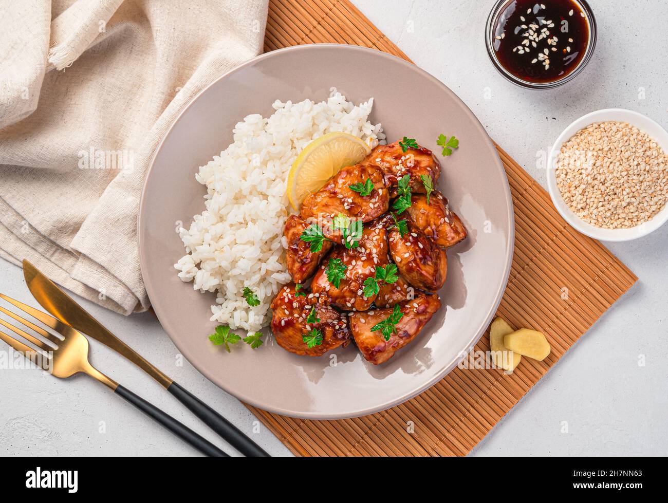 Teriyaki chicken with sesame seeds, rice and fresh parsley on a light background. Stock Photo
