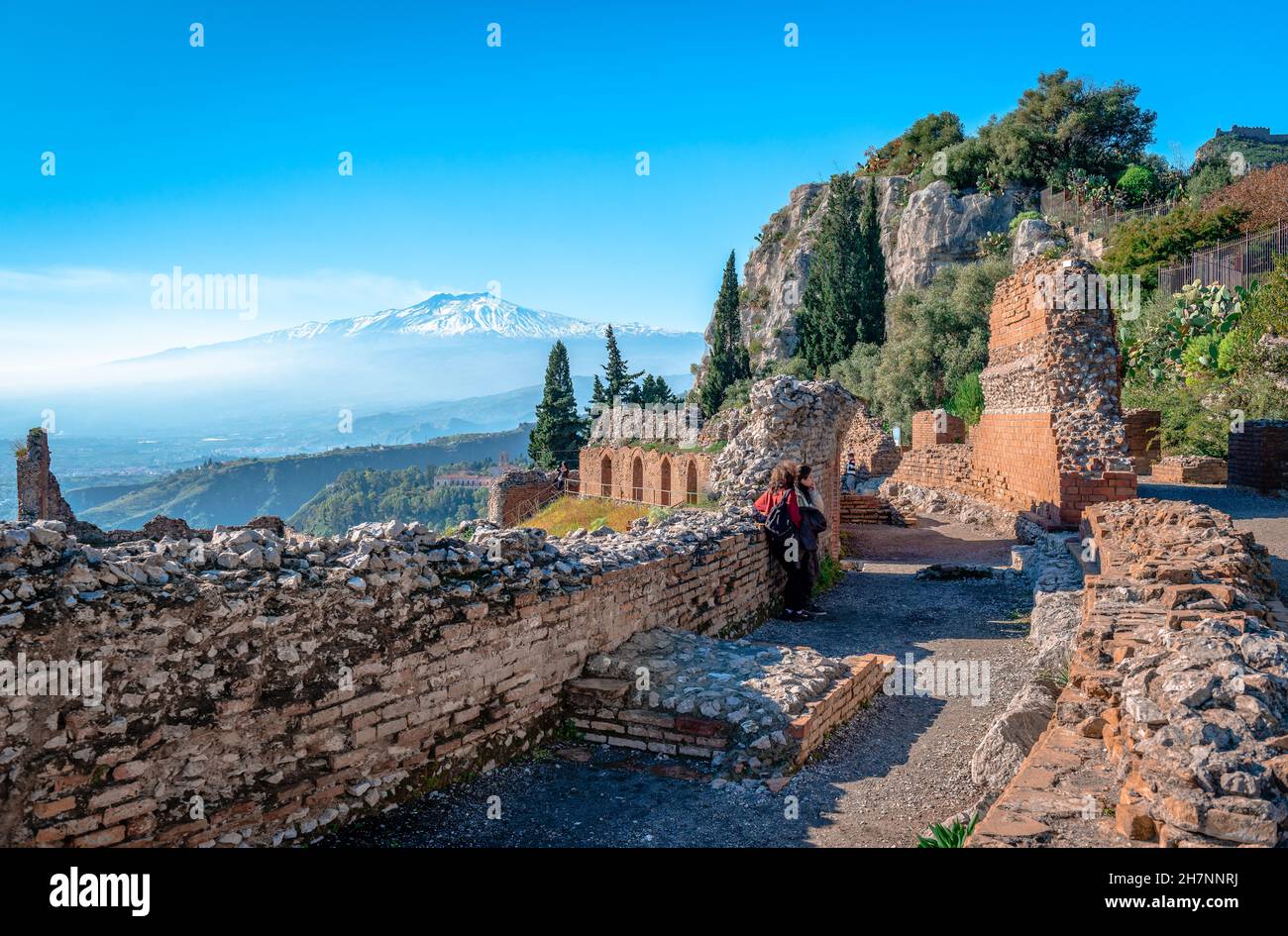 Via Teatro Greko, the ancient alley that leads to the Ancient Greek Theatre. The smoking foggy Mount Etna is in the background. Sicily, Italy. Stock Photo