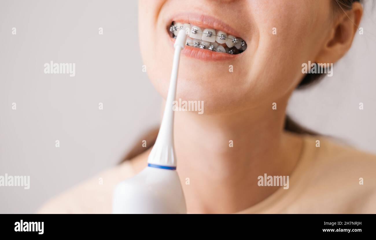 Smiling young unrecognizable woman with braces cleaning her teeth with oral irrigator. Stock Photo
