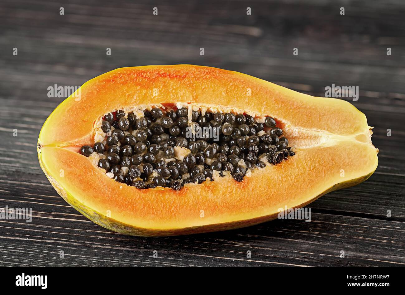 Half papaya on a wooden table. Papaya lies on dark boards with a blurred background. Stock Photo