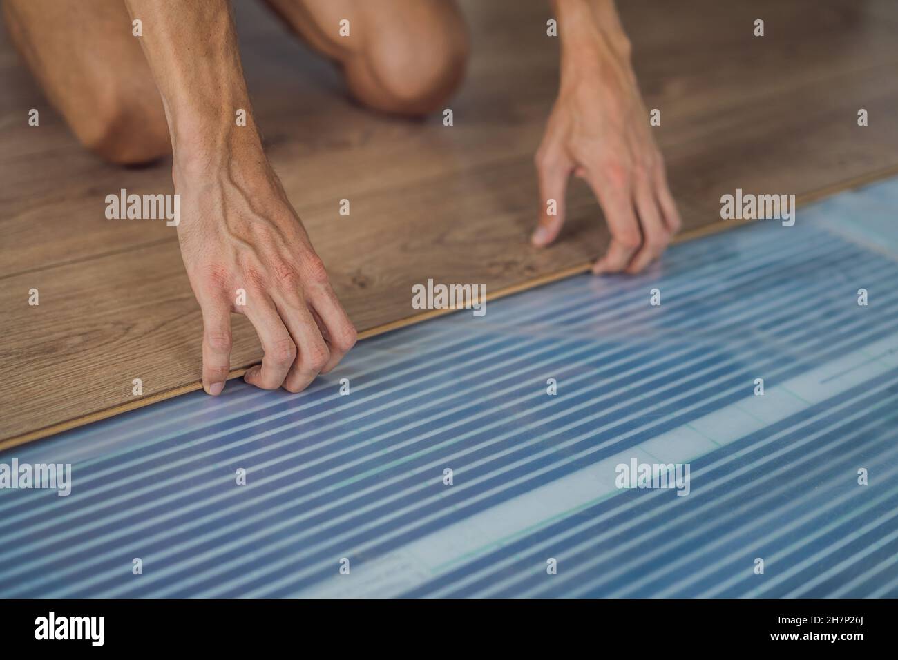 Man installing new wooden laminate flooring on a warm film floor