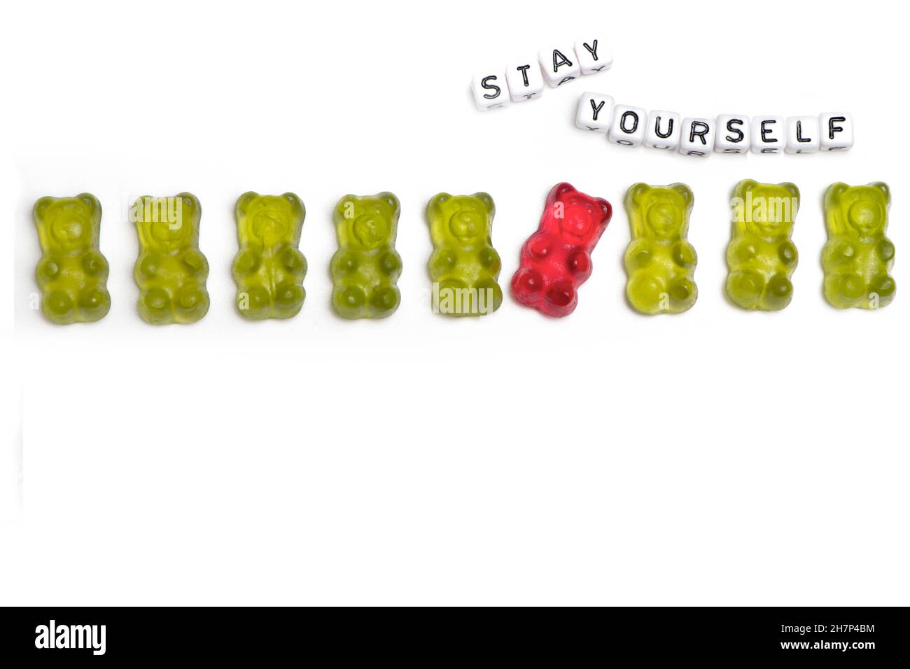 a row of green gummy bears in which a red guy behaves differently out of a concept for individuality and being different is isolated on a white backgr Stock Photo