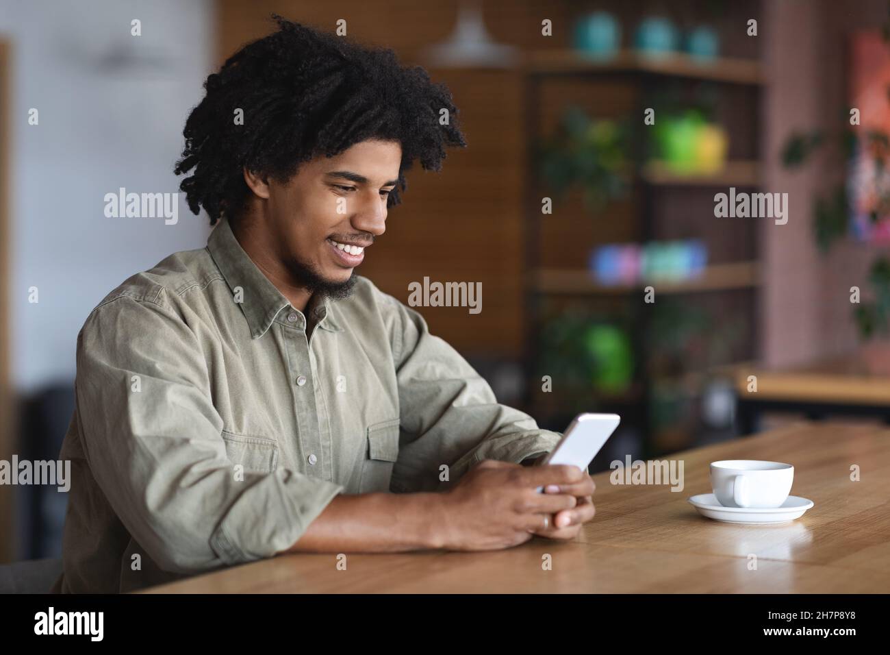 Young African American Guy Using Smartphone While Sitting At Tablet In Cafe Stock Photo