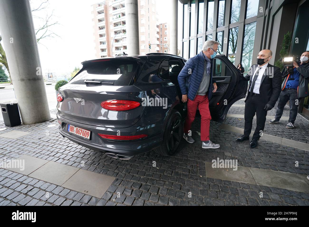 24 November 2021, Hamburg: Chauffeur Mazi Salimi (2nd from right) opens the door of the luxury SUV Bentley Bantayga Hybrid to a vaccinated person in front of the Empire Riverside Hotel at the port of Hamburg. On Wednesday, people who want to be vaccinated against Corona could be chauffeured to their appointment in a luxury car in Hamburg. After the vaccination in the Skyline Bar 20up on the 20th floor of the hotel, there was a great view over Hamburg as well as an alcohol-free cocktail. Several Hamburg companies wanted to use this action as an incentive for the vaccination against Corona. Phot Stock Photo