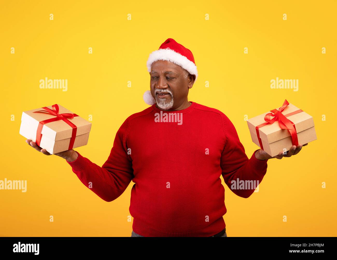 Senior black man in Santa hat holding Christmas gifts in both hands, celebrating New Year over orange background Stock Photo