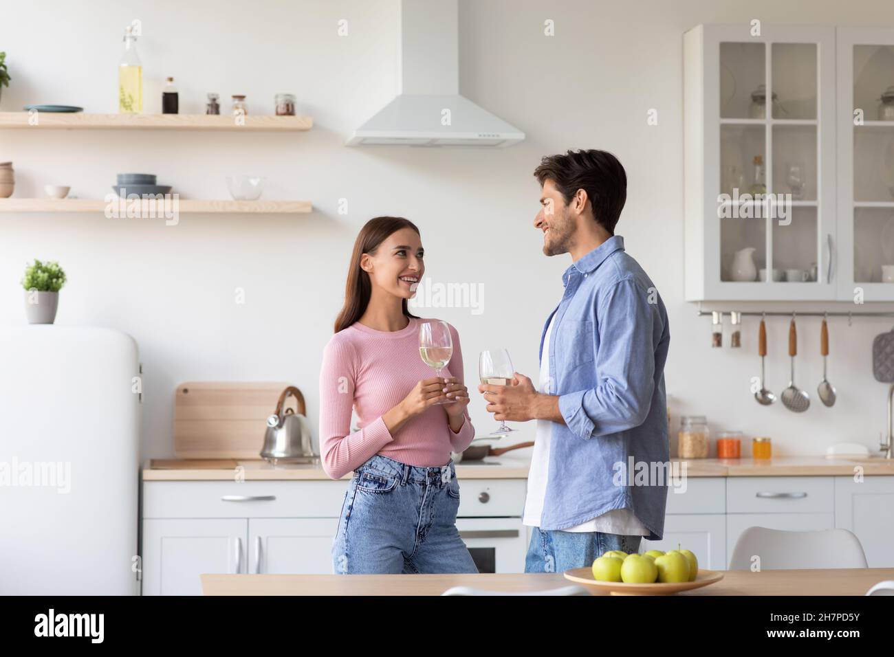 Smiling millennial caucasian family with glasses of wine in modern kitchen interior, celebrate anniversary Stock Photo