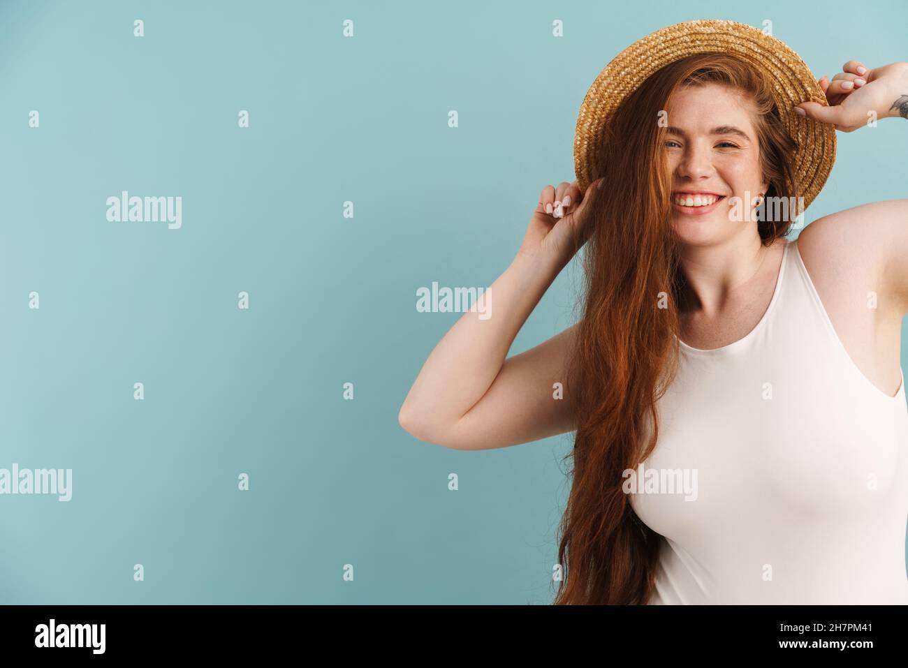 Young ginger woman in straw hat smiling and looking at camera isolated ...