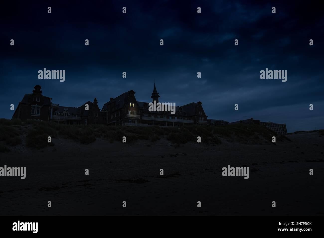 old spooky clinic in the dunes of berck sur mer, France. Creepy night photograph, two windows are mysteriously illuminated. Stock Photo