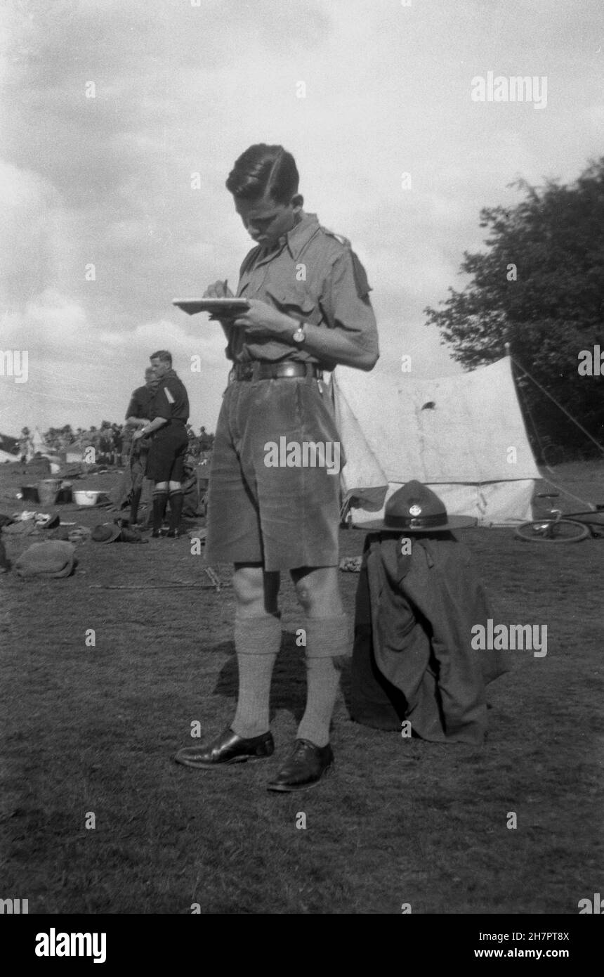 1935, historical, outside in a field, a scout in his uniform standing writing notes on a jotter pad at a scout camp at Ranmore on the North Downs, in the Surrey hills, England, UK. Stock Photo