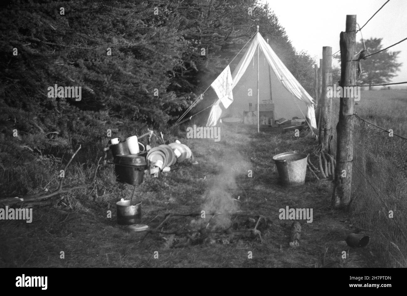 1937, historical, scout camp, a camp kitchen in a cleared area next to a wood and beside a fenced field, with a tent, fire and cooking utensils, Ranmore, North Downs, Surrey, England, UK. Stock Photo