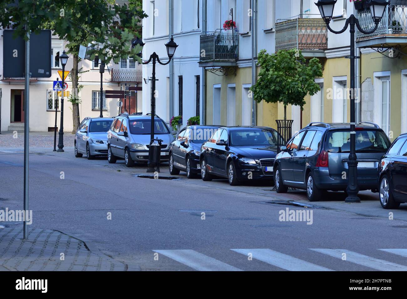 Passenger cars standing in a car park separated from the public road next to residential houses. Stock Photo