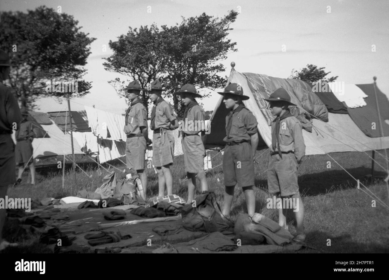 1938, historical, scout camp, outside in a field, several young boy scouts in their uniform and hats standing beside their personal kit layed out for a formal kit inspection, England, UK. Made from wool and flet, and worn by scout troops up to the 1960s, the traditional scout hat was also known as a campaign or 'lemon squeezer' hat. Stock Photo