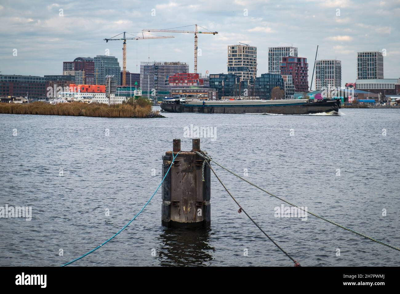 Cargo barge passes in front of large scale urban development on the waterfront of Amsterdam North. Stock Photo