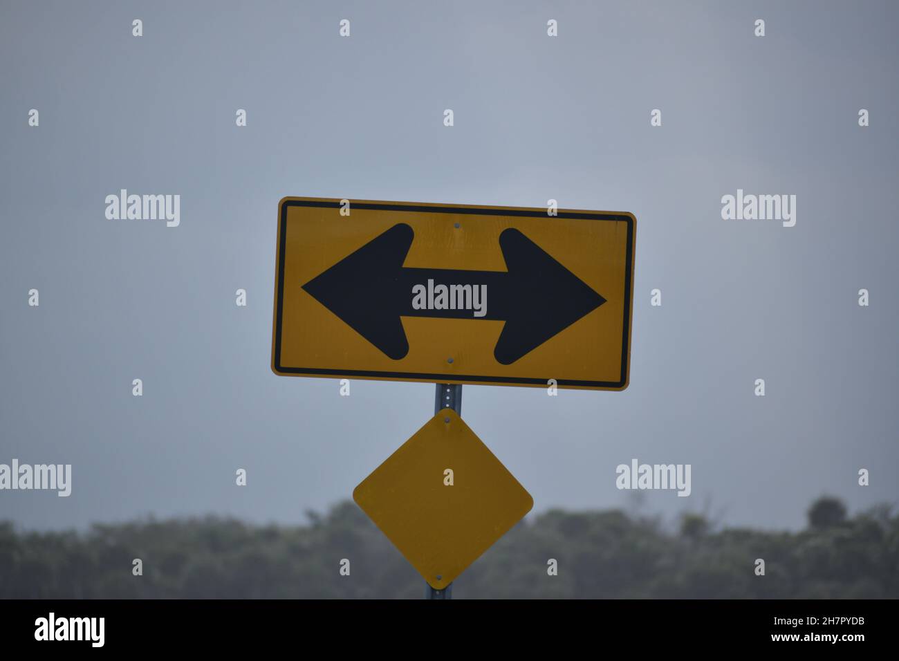 Black arrows on a yellow sign indicate traffic must turn. Stock Photo
