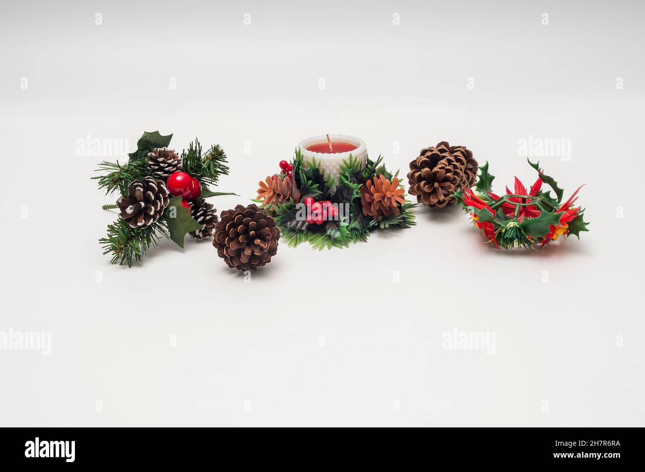 Plastic table-top or mantle-top Christmas decorations of a candle, pine cones, holly, and poinsettias. Stock Photo