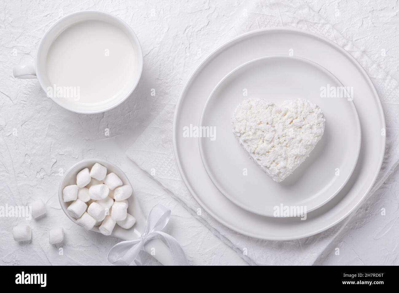 Heart shaped cottage cheese in a plate, milk and marshmallows on a white table Stock Photo