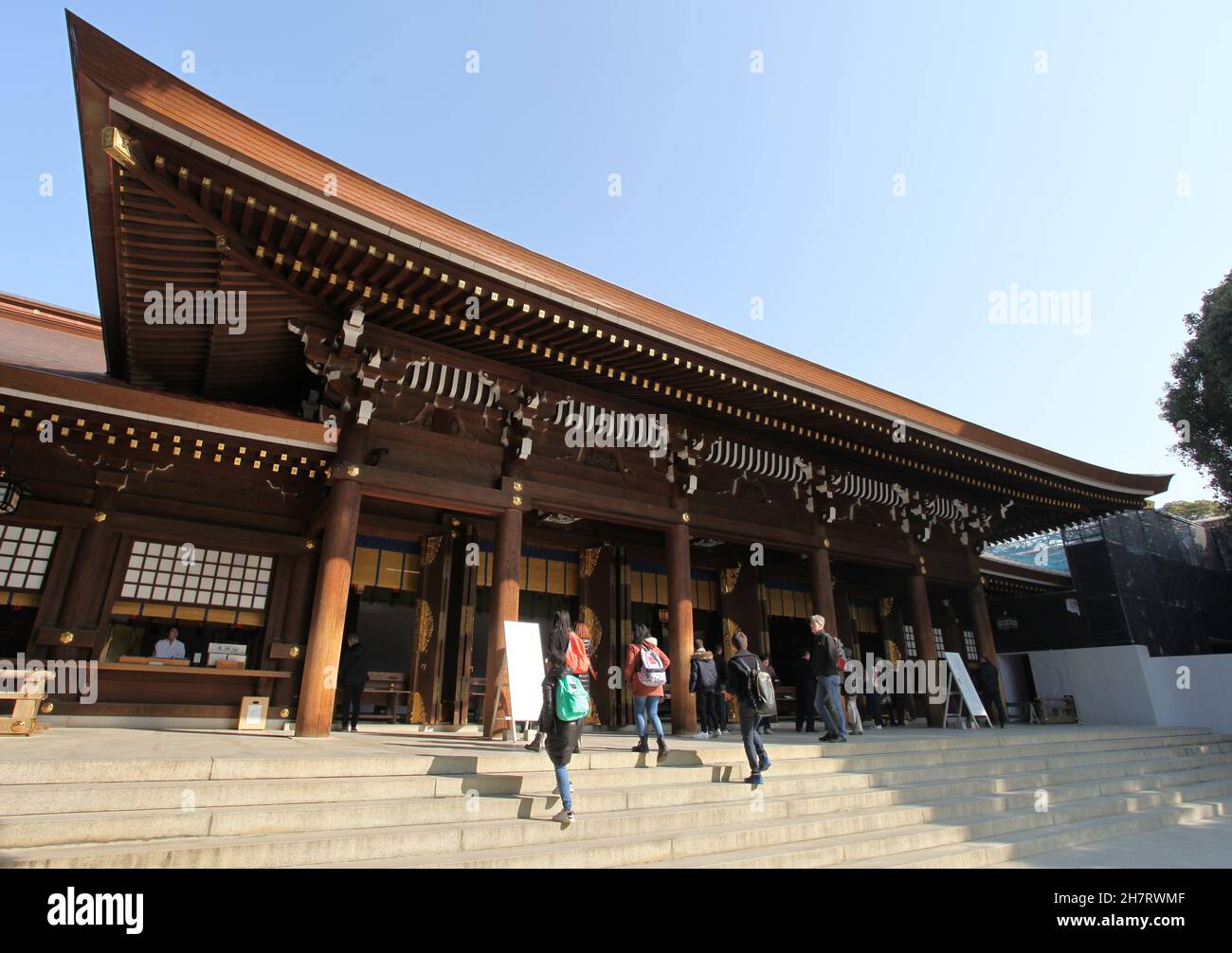 The Meiji Jingu Shrine in Shibuya City, Tokyo, Japan. The shrine is a Shinto shrine and is made of natural coloured wood. Several visitors are present. Stock Photo