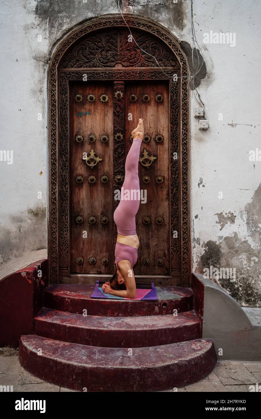 Young Caucasian woman doing yoga poses on a mat next to ancient wooden doors Stock Photo Alamy